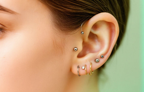 Curated ear with titanium studs and gold hoops across the lobe, helix and conch