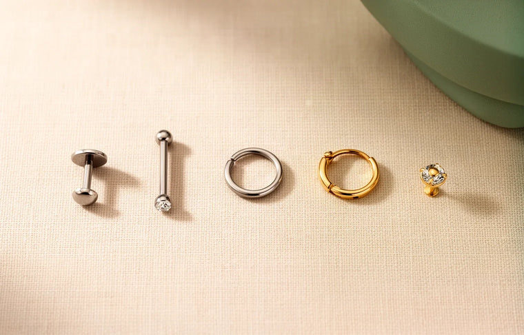 Piercing jewellery types laid out: labret, barbell, seamless ring, clicker and stud in titanium and gold