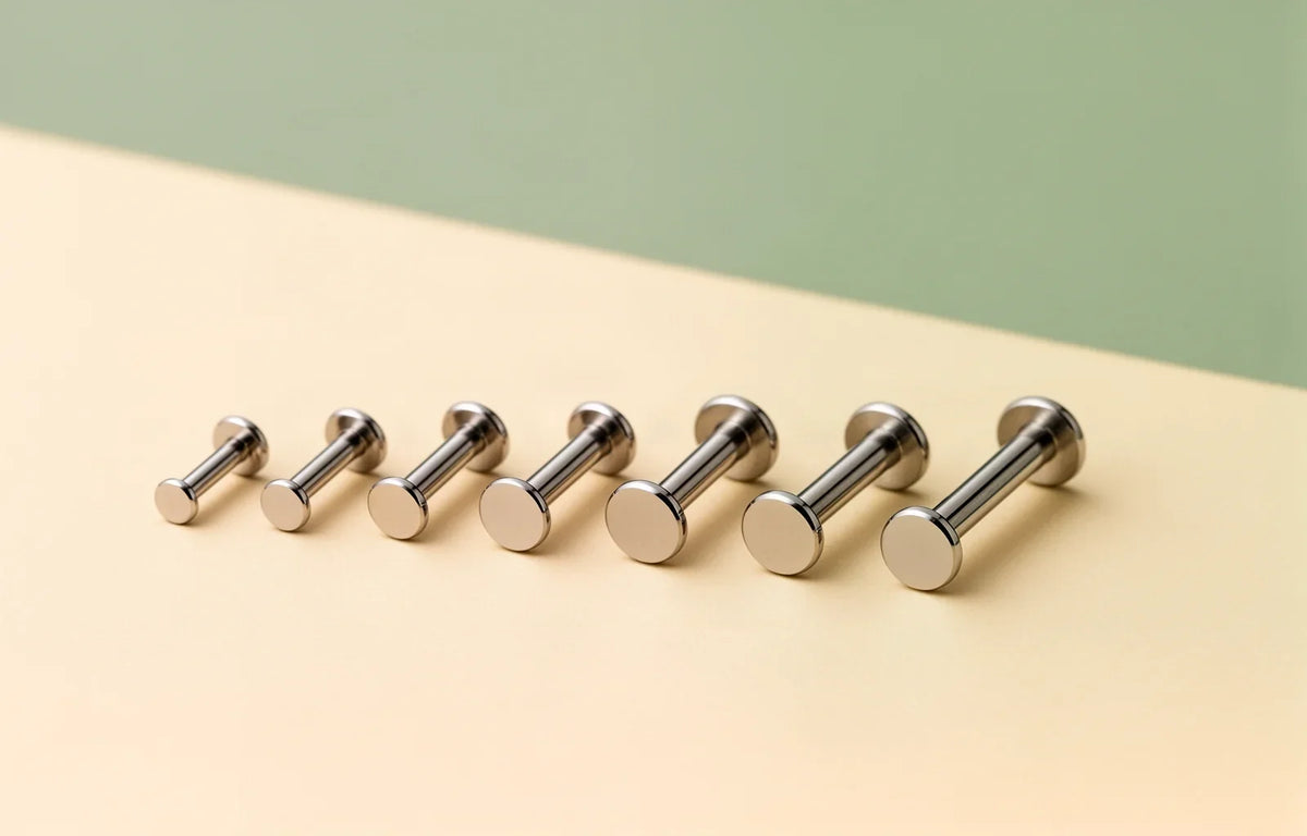 A row of titanium flat-back labret bars in different gauges and lengths on a cream surface